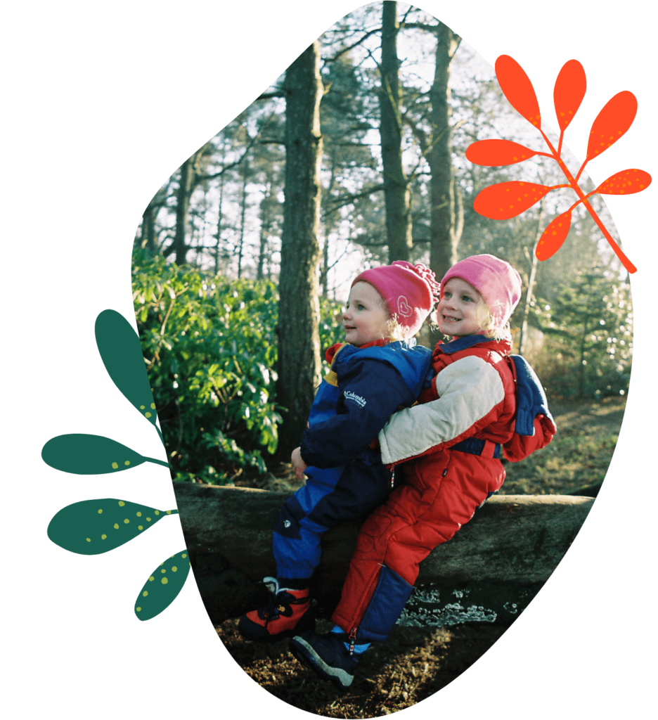two happy girls dress up warm sit on a tree trunk