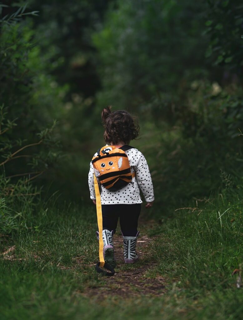 Little girl walking in woods with back oak on