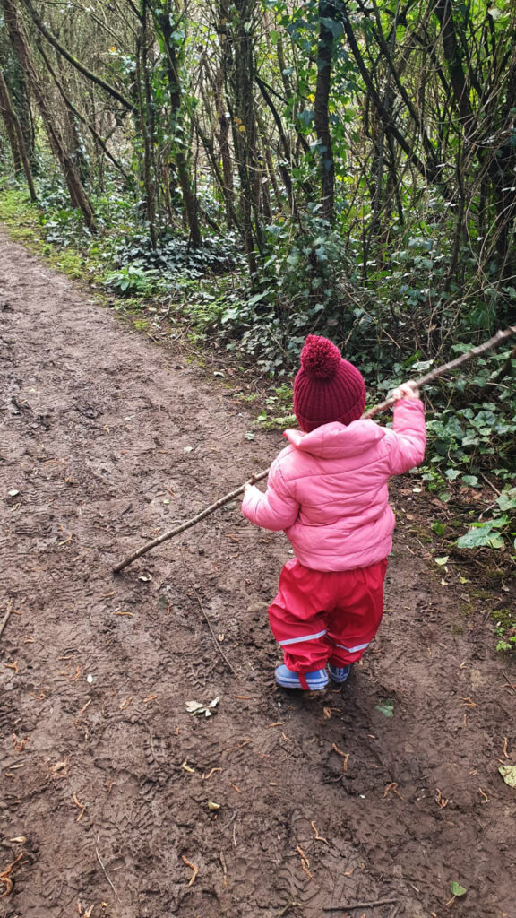 Little girls walks along a nature path holding a stick.