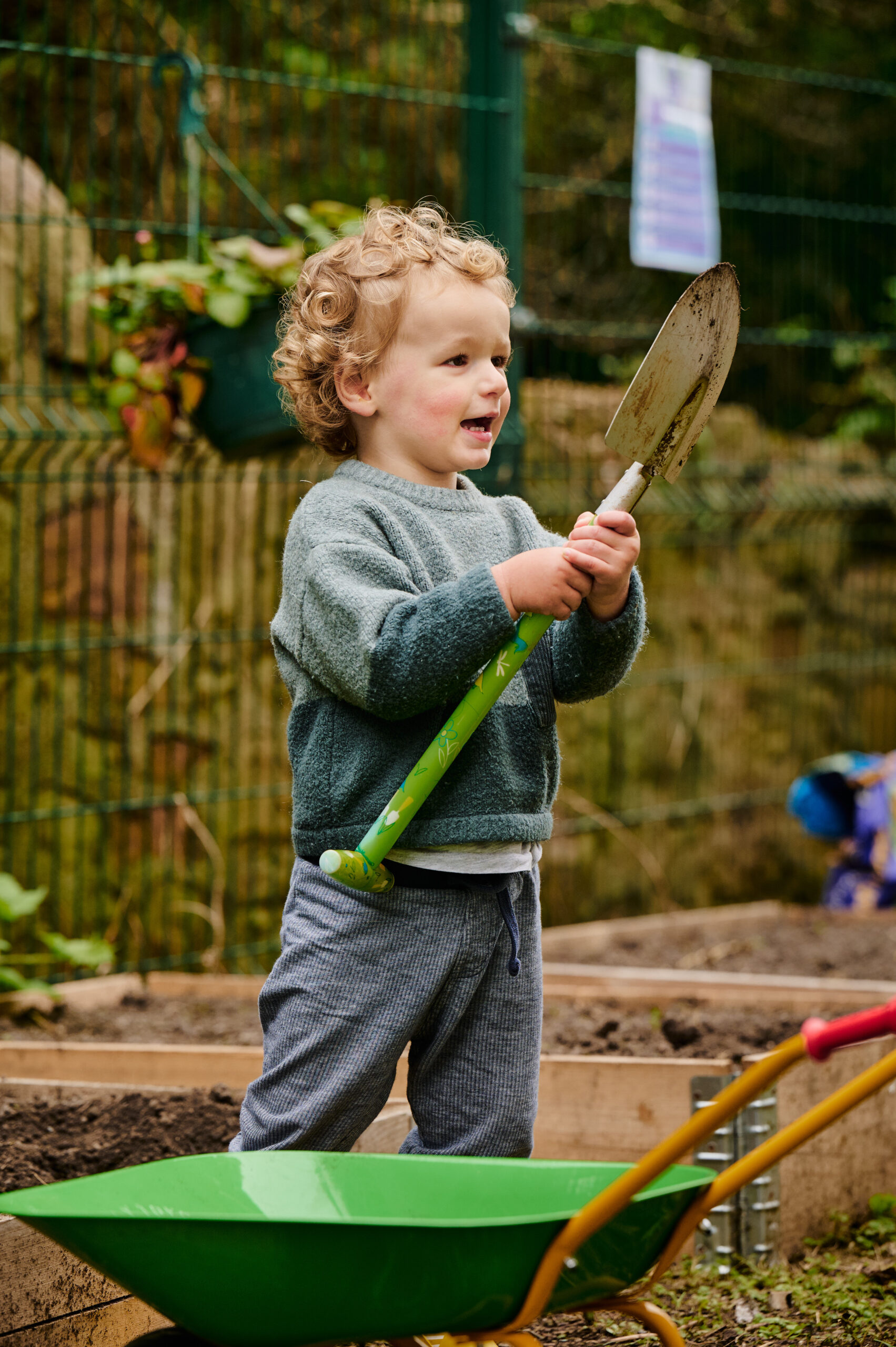 boy with curly hair is holding a spade and getting ready to do some digging